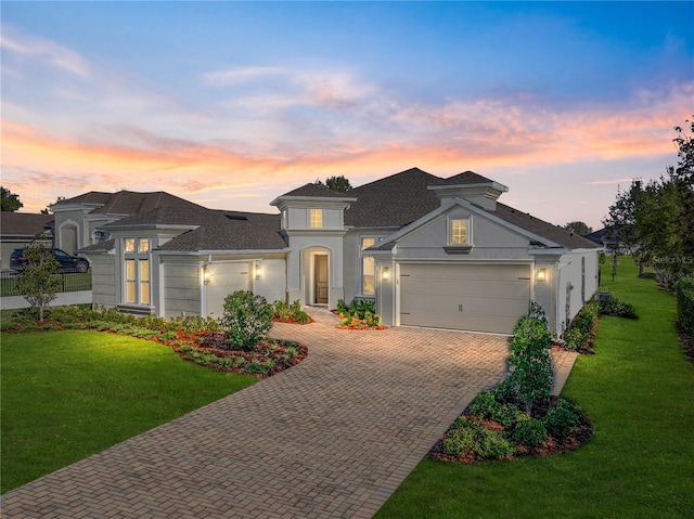 view of front of property with stucco siding, decorative driveway, a yard, an attached garage, and a shingled roof