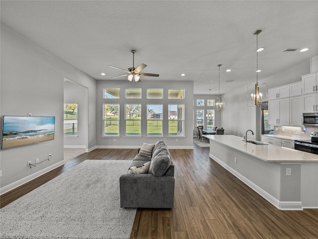 living room featuring dark wood finished floors, recessed lighting, ceiling fan with notable chandelier, and baseboards