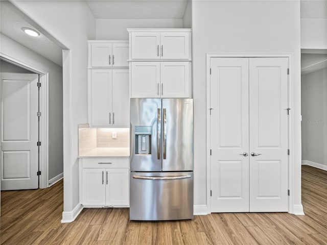 kitchen featuring decorative backsplash, white cabinets, light wood-style floors, and stainless steel fridge