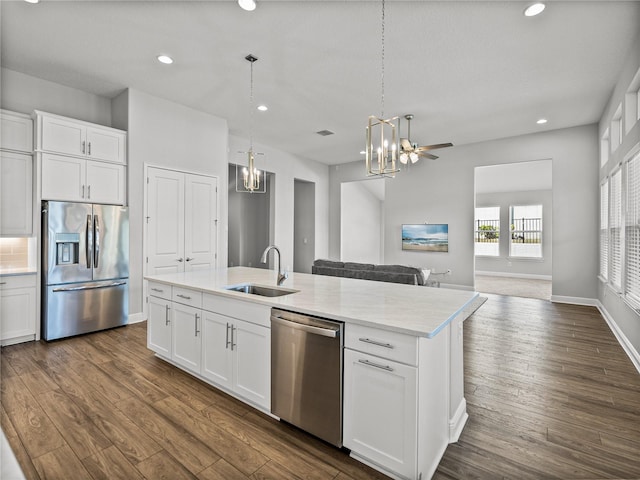 kitchen featuring an island with sink, a sink, dark wood-style floors, stainless steel appliances, and an inviting chandelier