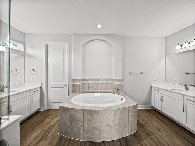 full bathroom featuring a garden tub, two vanities, wood finished floors, and a sink