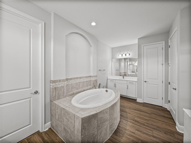 bathroom with wood finished floors, a bath, and vanity