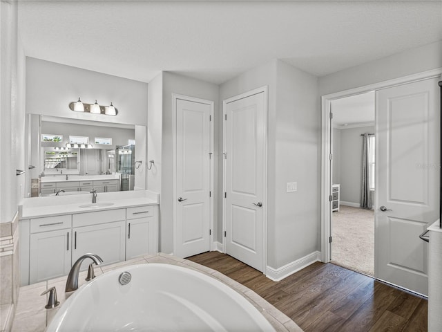 full bath featuring baseboards, wood finished floors, vanity, and a bath