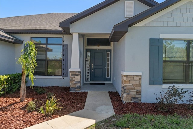 view of exterior entry with a shingled roof and stucco siding