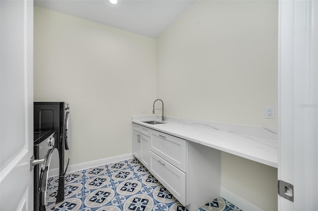 laundry area with baseboards, light tile patterned floors, washer and dryer, cabinet space, and a sink