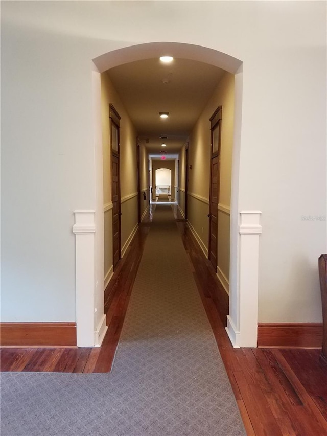 hall with baseboards, arched walkways, and dark wood-type flooring