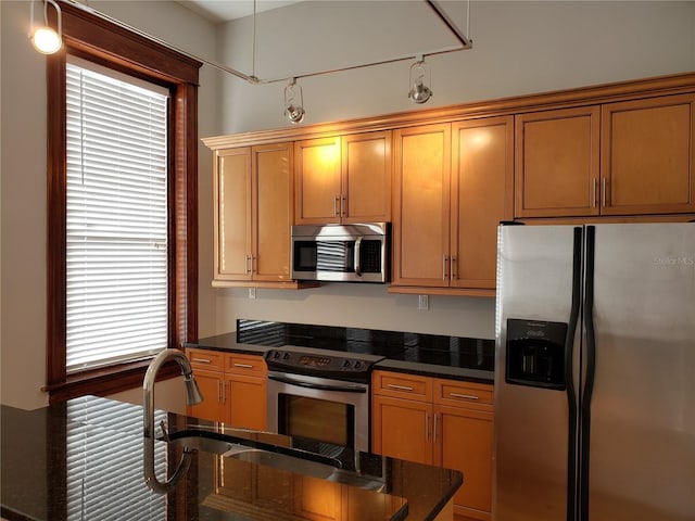 kitchen featuring dark stone counters, brown cabinets, appliances with stainless steel finishes, and a sink