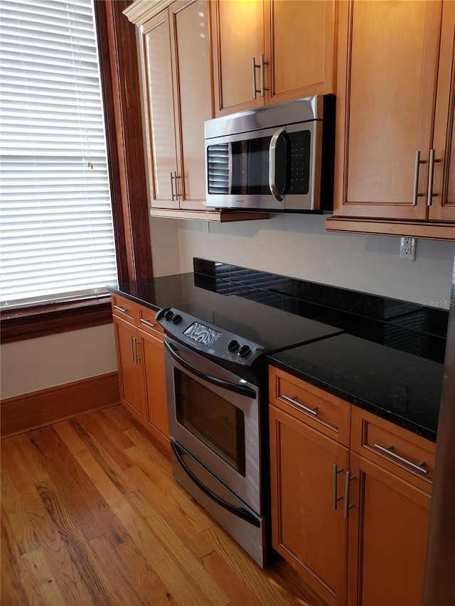 kitchen with dark stone counters, baseboards, light wood-style floors, and appliances with stainless steel finishes