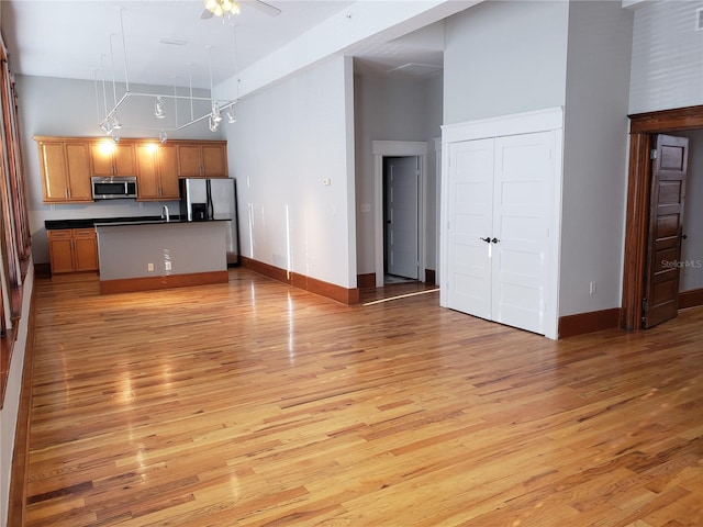 kitchen featuring dark countertops, light wood-style floors, appliances with stainless steel finishes, rail lighting, and a towering ceiling