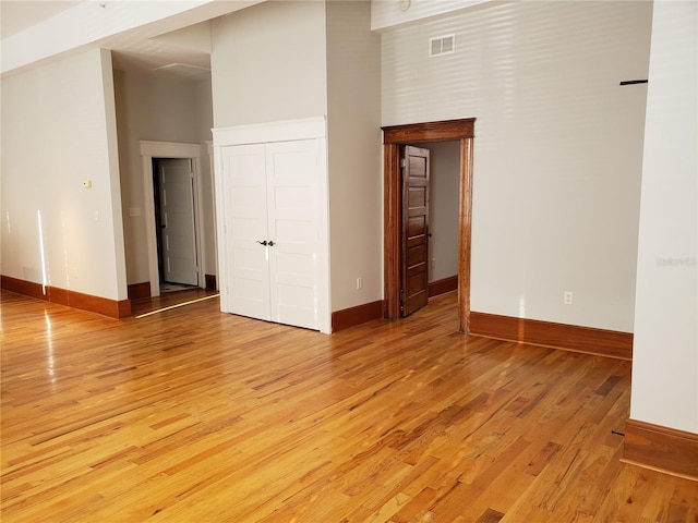 empty room featuring baseboards, visible vents, a towering ceiling, and light wood-type flooring