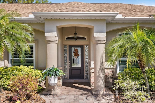 property entrance with stucco siding and a shingled roof