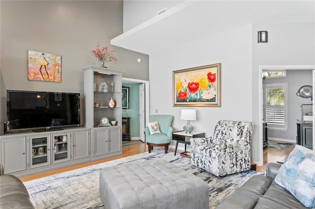 living room featuring visible vents, a high ceiling, baseboards, and light wood-type flooring