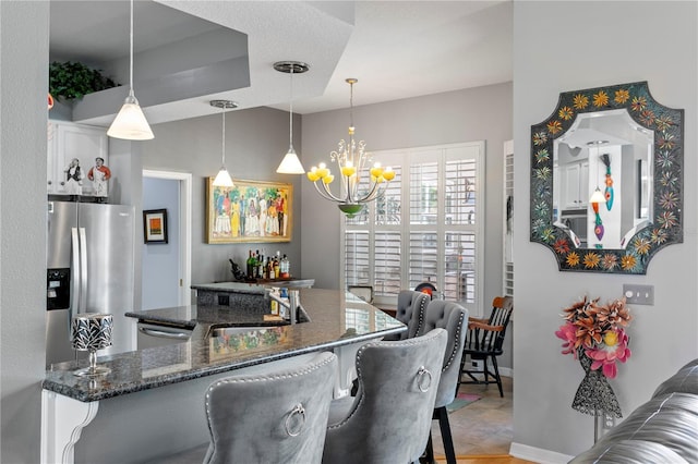 kitchen with a breakfast bar area, dark stone countertops, an inviting chandelier, stainless steel appliances, and a sink