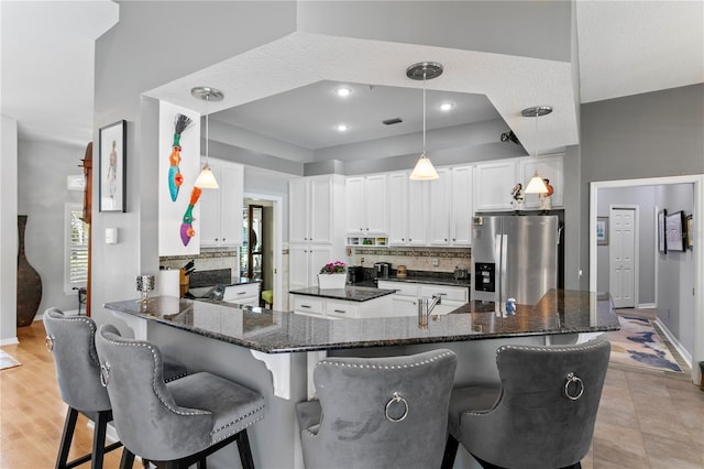 kitchen featuring backsplash, a kitchen bar, dark stone countertops, stainless steel refrigerator with ice dispenser, and white cabinets