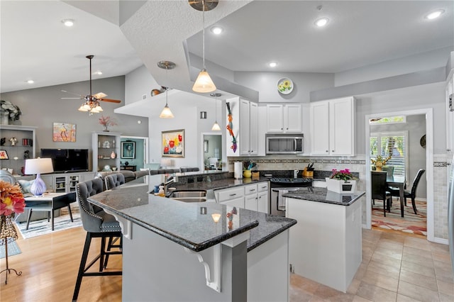 kitchen featuring a sink, white cabinetry, stainless steel appliances, dark stone counters, and a peninsula