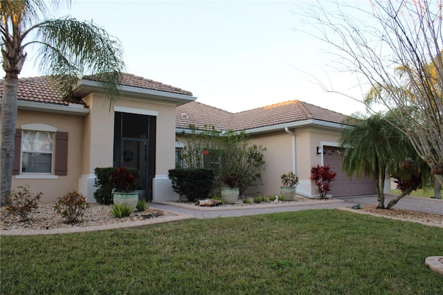 view of front of house with stucco siding, a garage, a front yard, and a tiled roof