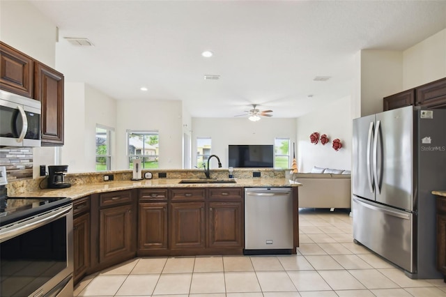 kitchen featuring a sink, light stone counters, open floor plan, appliances with stainless steel finishes, and light tile patterned floors