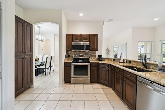 kitchen with tasteful backsplash, light tile patterned floors, appliances with stainless steel finishes, arched walkways, and a sink