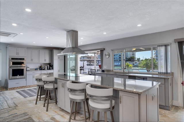 kitchen featuring a spacious island, black electric stovetop, double oven, island exhaust hood, and a sink