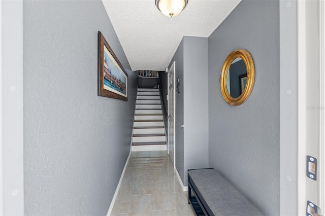 hallway featuring stairway, baseboards, a textured ceiling, and a textured wall