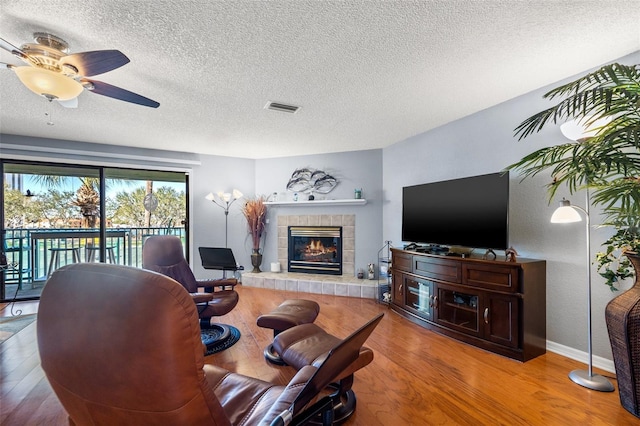 living area featuring wood finished floors, visible vents, a ceiling fan, a textured ceiling, and a tiled fireplace