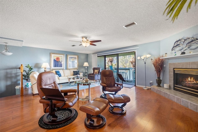 living area with visible vents, a ceiling fan, a textured ceiling, wood finished floors, and a tile fireplace