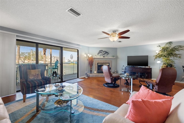 living area featuring visible vents, a fireplace, wood finished floors, and a ceiling fan