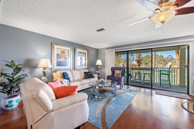 living room with wood finished floors, visible vents, ceiling fan, a textured ceiling, and a textured wall