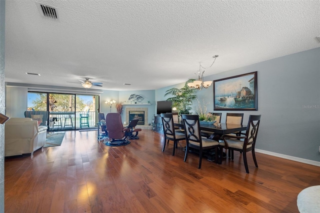 dining space with visible vents, ceiling fan with notable chandelier, a fireplace, and wood finished floors