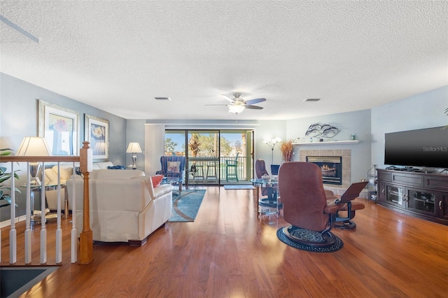 living room with ceiling fan, visible vents, wood finished floors, and a tile fireplace