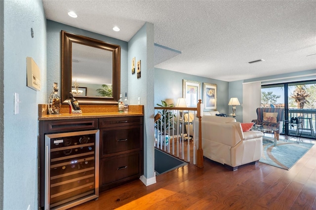 living room featuring wood finished floors, beverage cooler, visible vents, a textured ceiling, and a textured wall