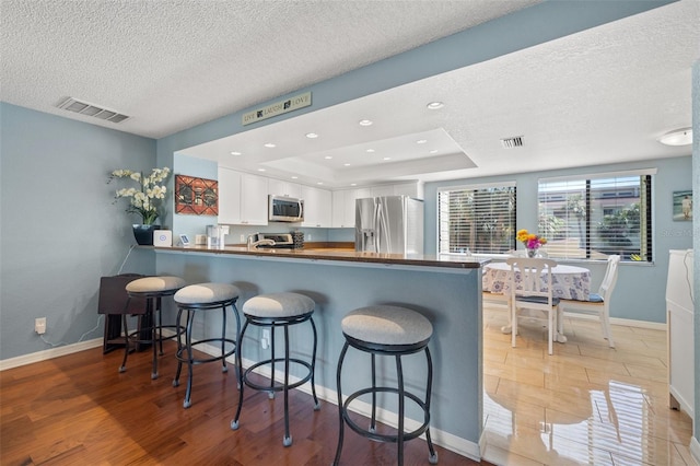 kitchen with a tray ceiling, visible vents, appliances with stainless steel finishes, and white cabinetry