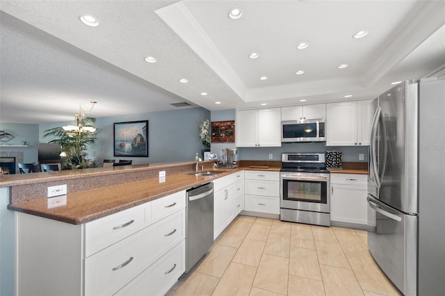 kitchen with dark stone countertops, a tray ceiling, a peninsula, a sink, and appliances with stainless steel finishes