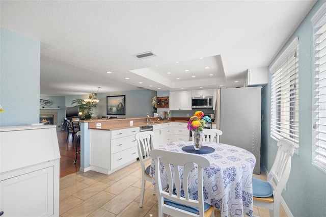 dining area with wood finish floors, visible vents, a tray ceiling, recessed lighting, and a lit fireplace