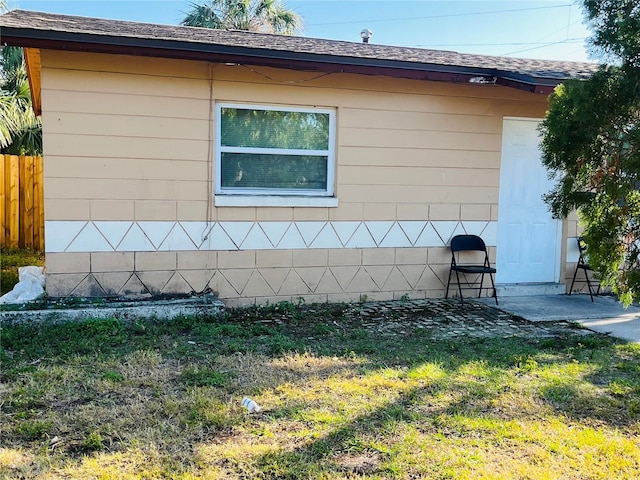 view of home's exterior featuring a yard, a shingled roof, and fence