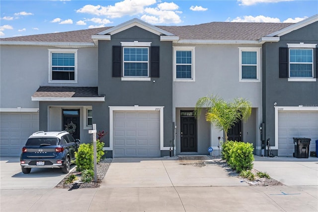 townhome / multi-family property featuring a garage, driveway, a shingled roof, and stucco siding
