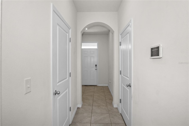 hall with arched walkways, light tile patterned flooring, and baseboards