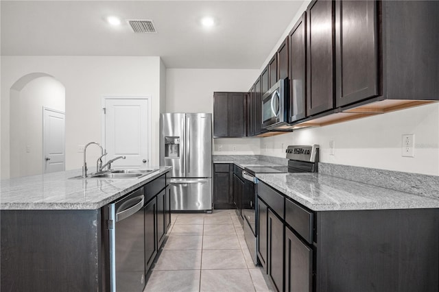 kitchen with stainless steel appliances, visible vents, a sink, arched walkways, and a center island with sink
