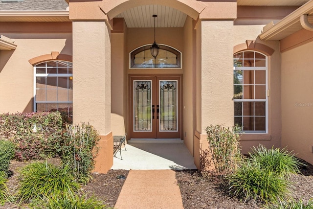 entrance to property with a shingled roof, french doors, and stucco siding