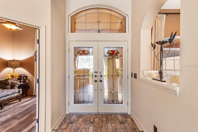 foyer entrance featuring brick floor, french doors, baseboards, and arched walkways