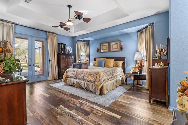 bedroom with a tray ceiling, access to outside, wood finished floors, and french doors