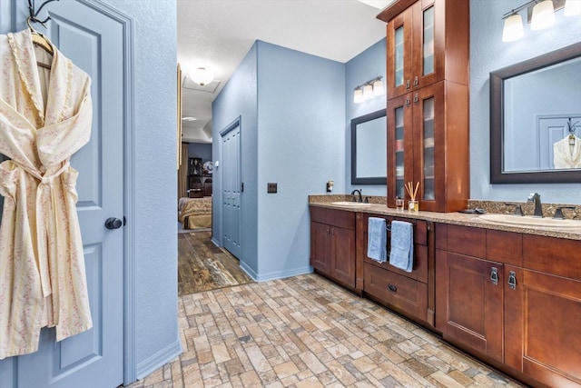 full bath with double vanity, connected bathroom, baseboards, and a sink