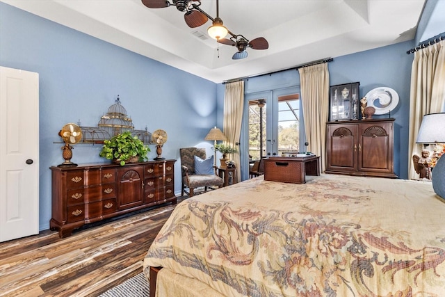 bedroom featuring access to exterior, a tray ceiling, wood finished floors, and visible vents