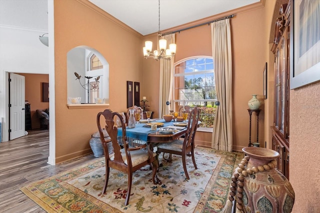 dining room with wood finished floors, baseboards, an inviting chandelier, a high ceiling, and crown molding