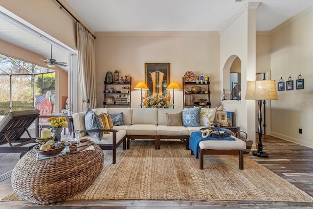 living area with crown molding, wood finished floors, baseboards, and arched walkways