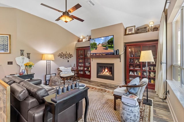 living area featuring a glass covered fireplace, lofted ceiling, wood finished floors, and visible vents