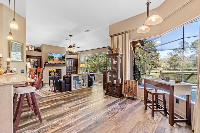 dining area with ceiling fan, visible vents, a warm lit fireplace, and wood finished floors