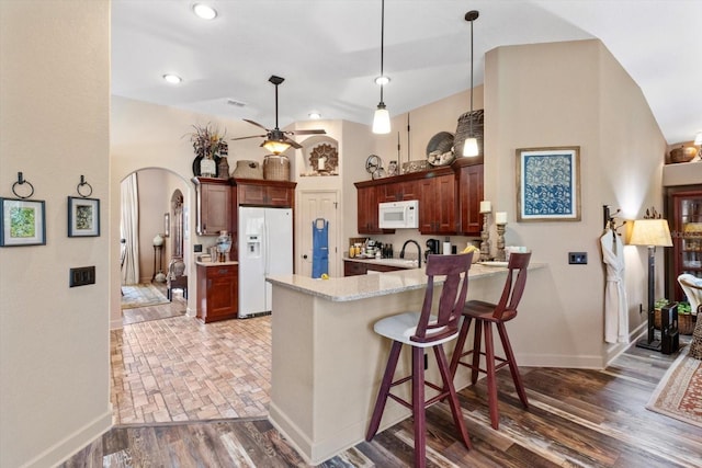 kitchen with a peninsula, wood finished floors, arched walkways, white appliances, and a ceiling fan