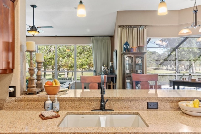 kitchen with hanging light fixtures, light stone counters, ceiling fan, and a sink