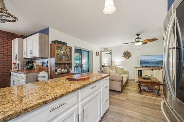 kitchen with light stone counters, a ceiling fan, light wood finished floors, white cabinetry, and stainless steel fridge